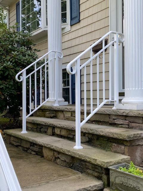 White handrails on stone steps leading up to a house with white columns.