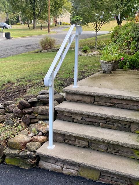 White handrail on stone steps leading to a house entrance. Green lawn and street in background.
