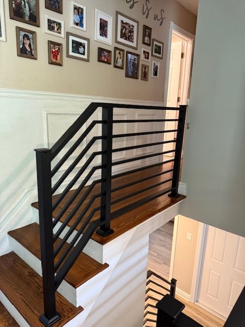 Black metal railing installed on wooden stairs, leading to a hallway with framed photos on the wall.