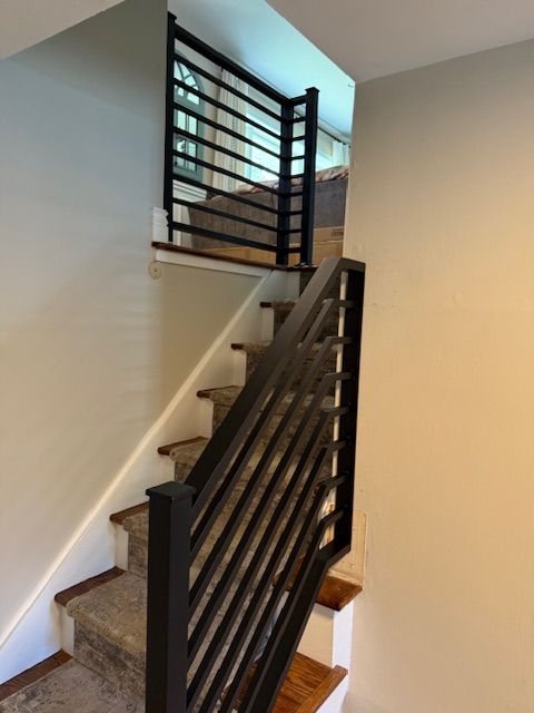 Staircase with black metal railing, leading up to a landing. Beige walls and carpeted stairs.