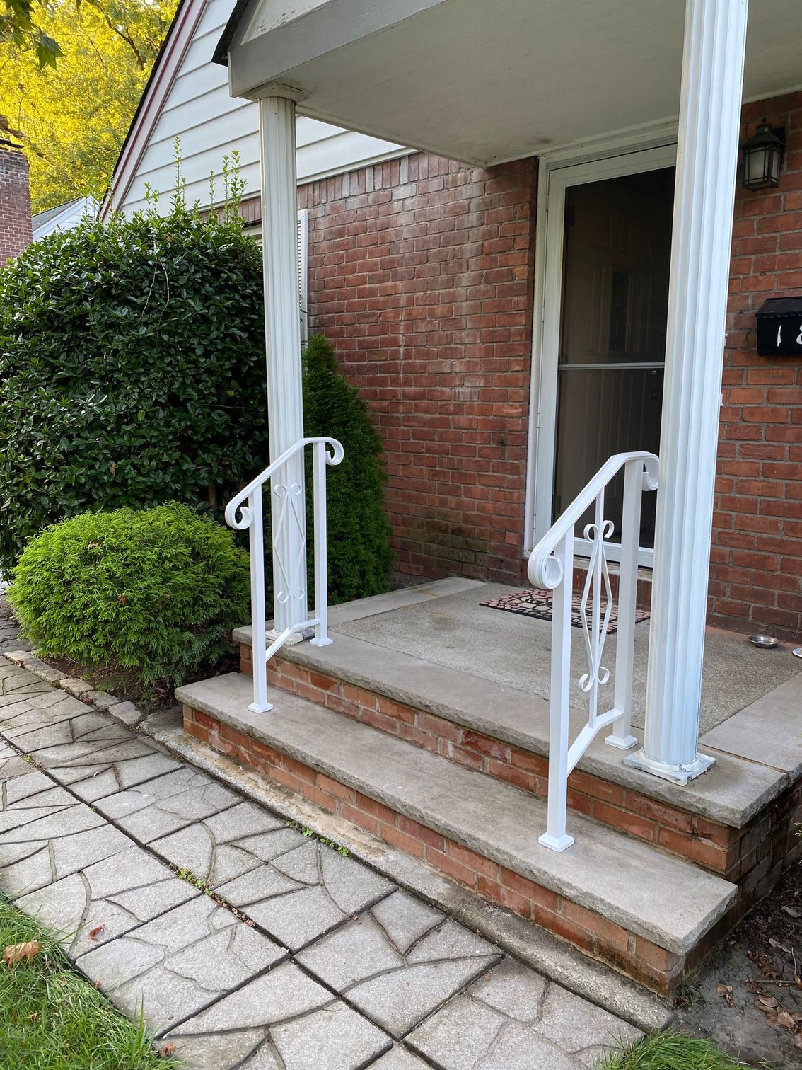 There is a white railing on the porch of a brick house.
