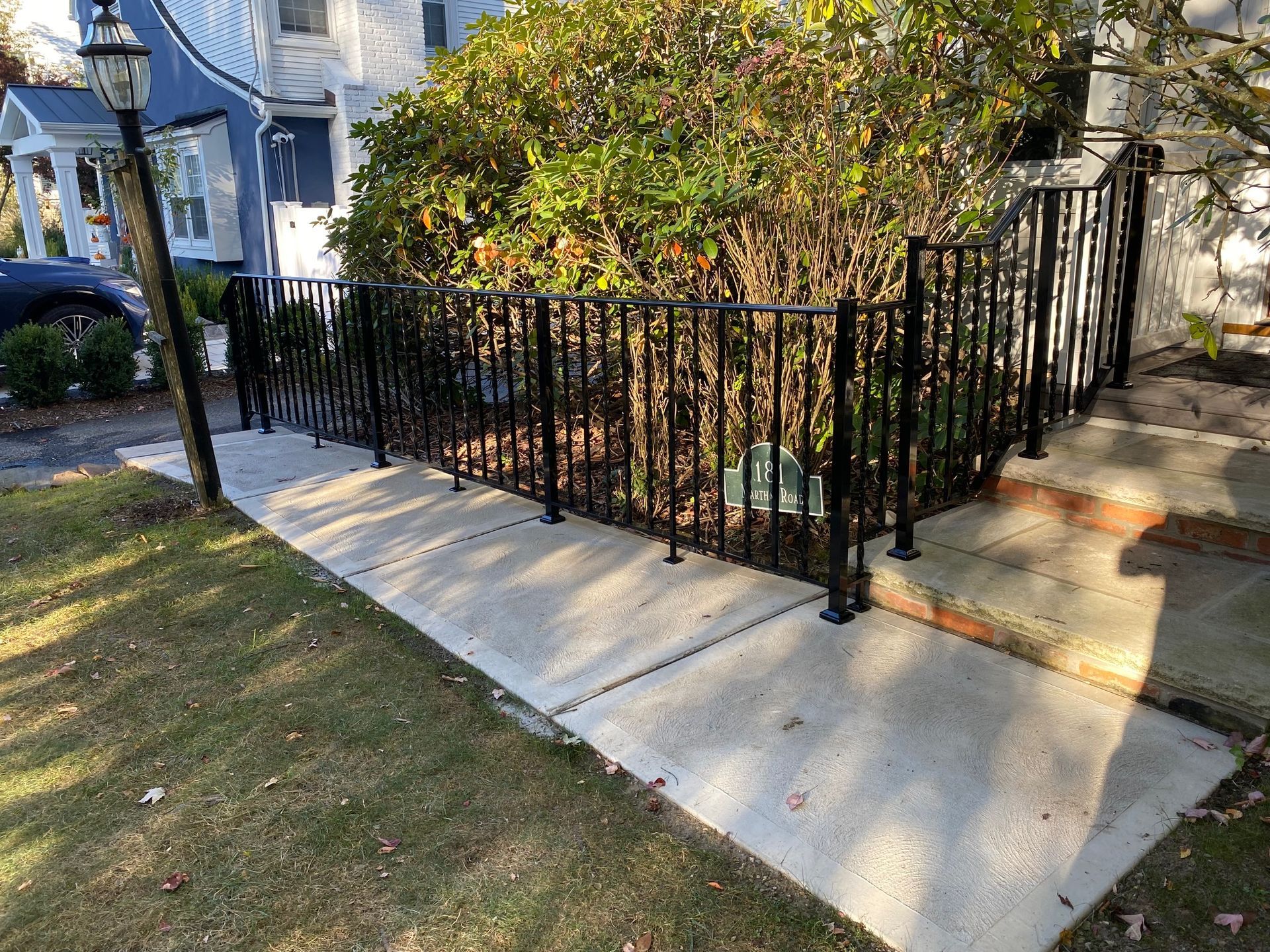 A wrought iron fence surrounds a concrete walkway leading to a house.