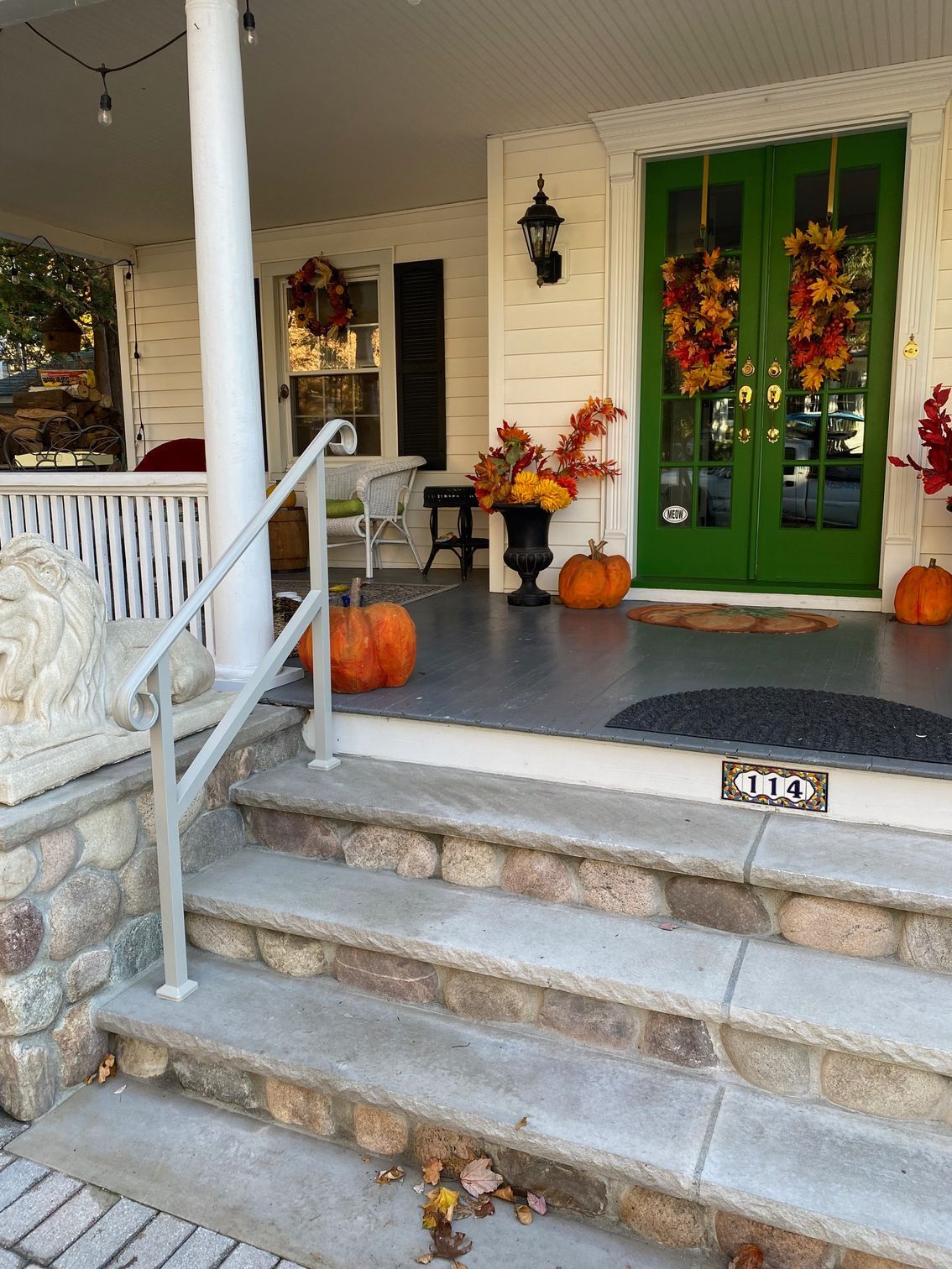 A porch decorated for fall with pumpkins , leaves and a lion statue.