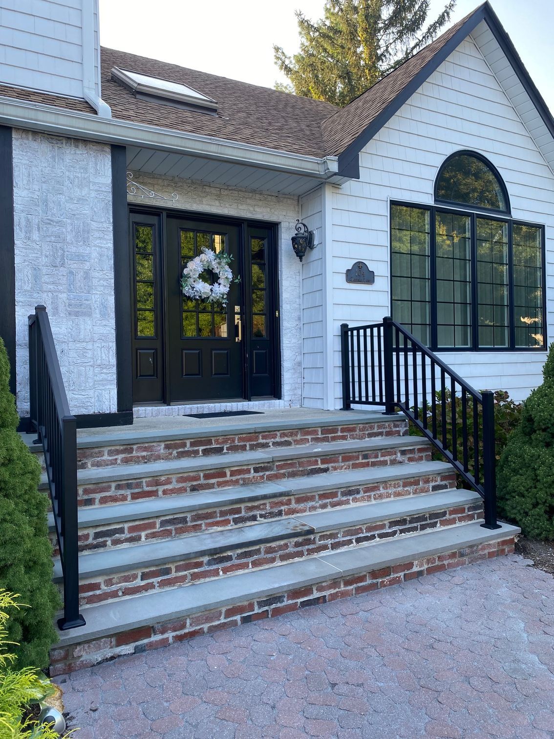The front of a white house with a black door and brick steps.