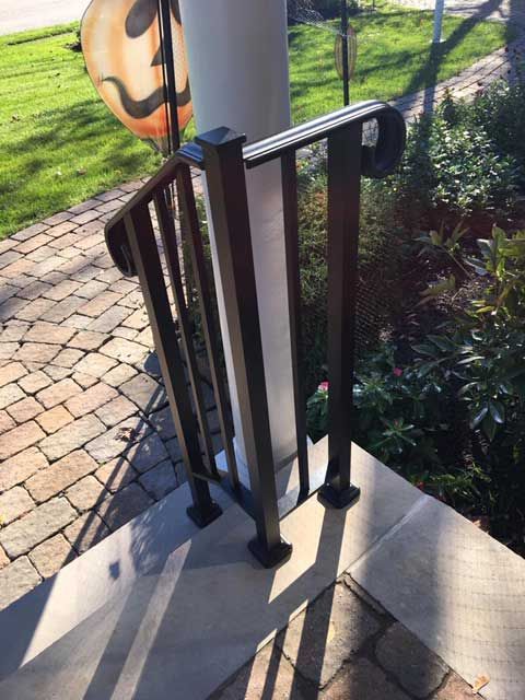 Black metal handrail on brick steps next to a white pillar, with a pumpkin decoration in the background.
