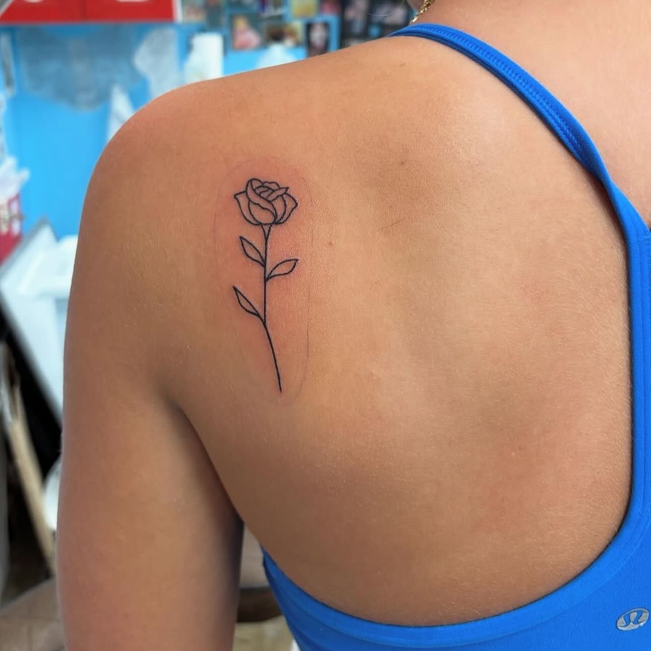 A person's shoulder with a small, black outline of a rose tattoo