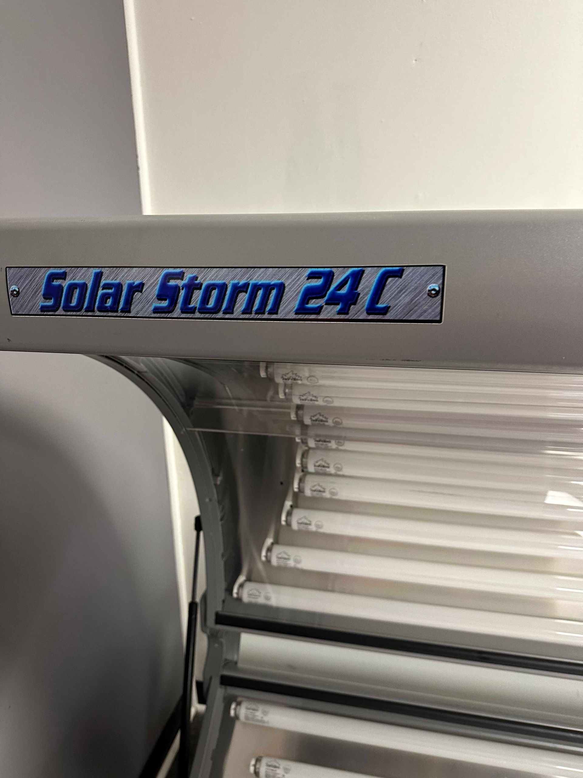 Solar Storm 24C tanning bed; silver frame with blue text, fluorescent lights visible below.