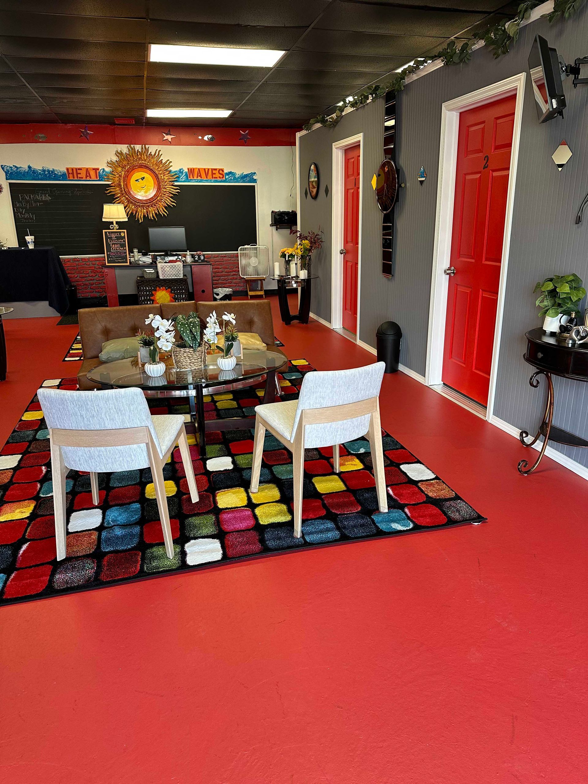 Colorful, eclectic room with a patterned rug, red floor, gray walls, and red doors. Two chairs face a low table.