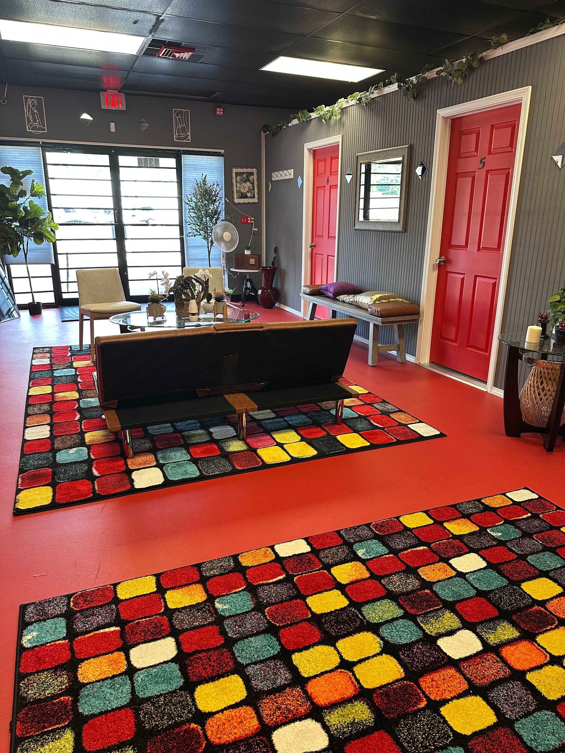 Brightly colored rugs in a waiting room with red doors, a black couch, and a large window.
