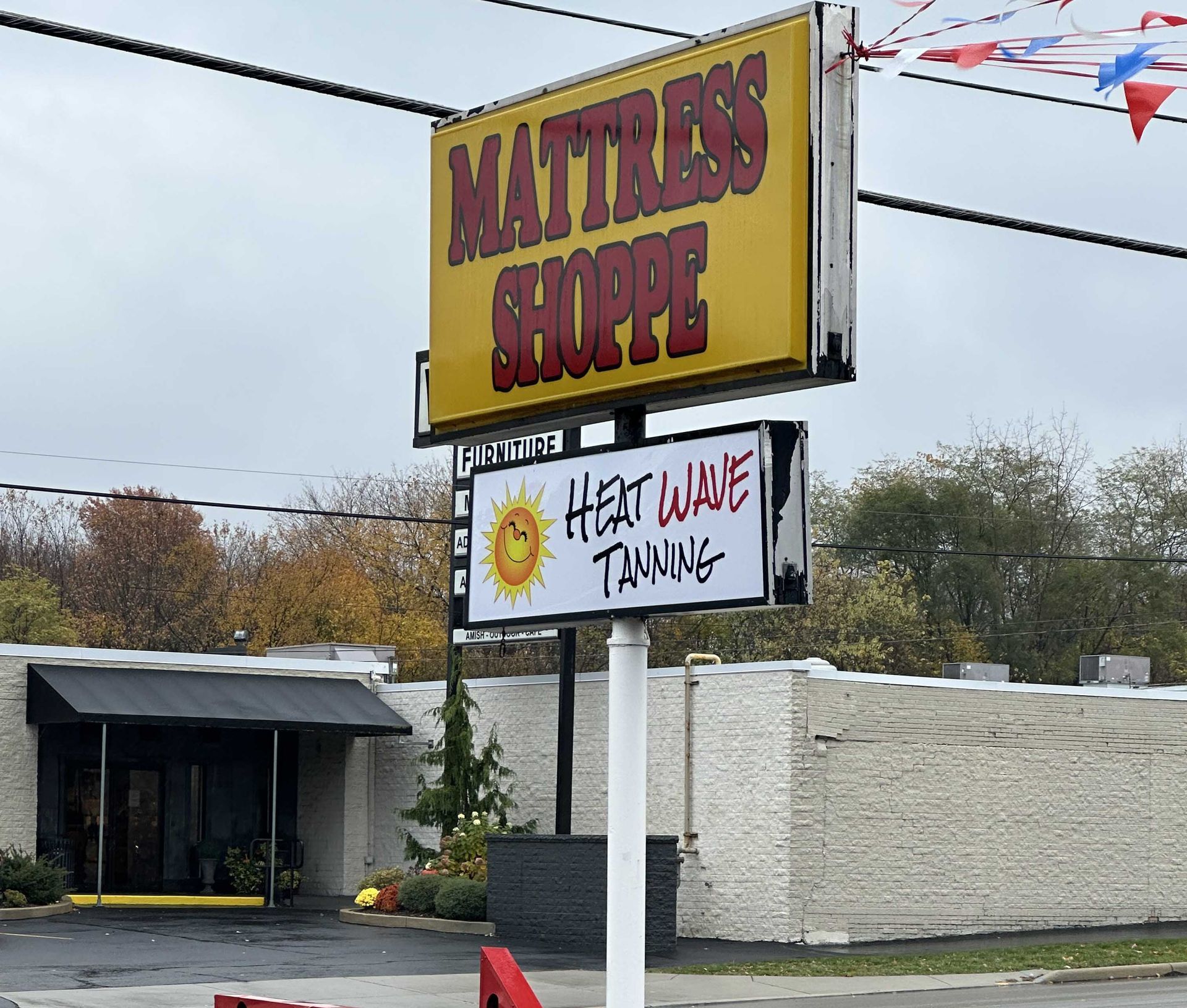 Sign for a Mattress Shoppe and Heat Wave Tanning business. Yellow sign on a cloudy day.