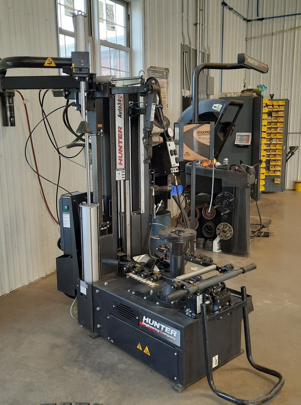 A black Hunter brand tire changing machine stands in an industrial shop with a tool rack in the background.