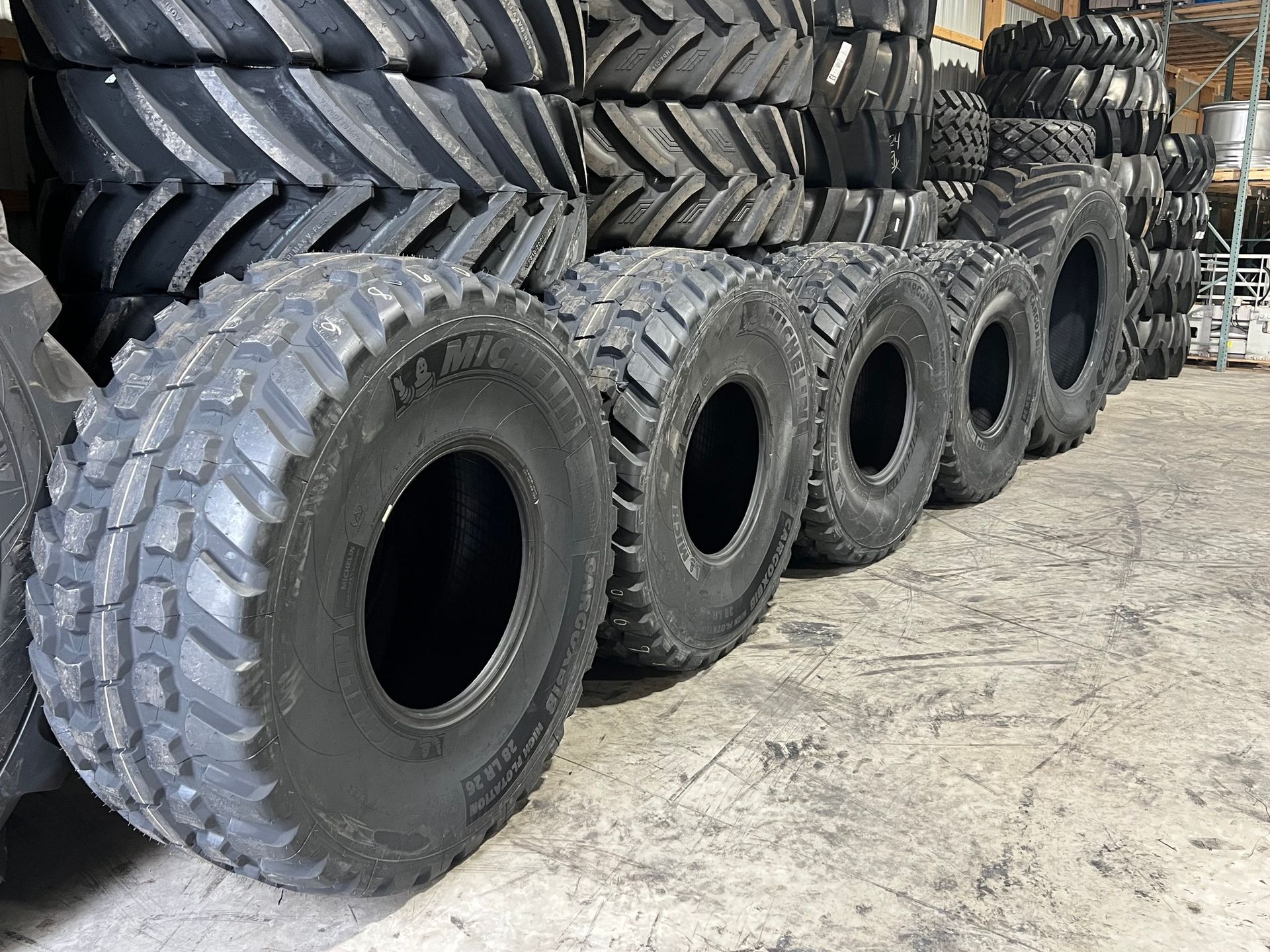 Row of large, black agricultural tires; other tires stacked in background; interior setting.