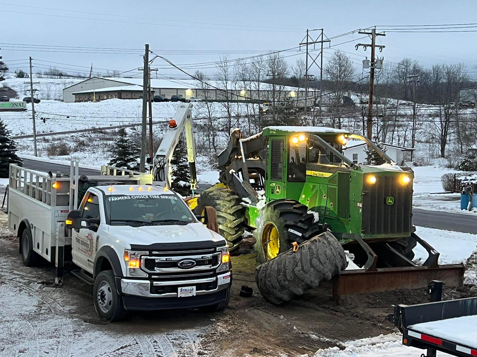 White truck and green John Deere tractor working on a snowy day. Utility truck is raised up near power lines.