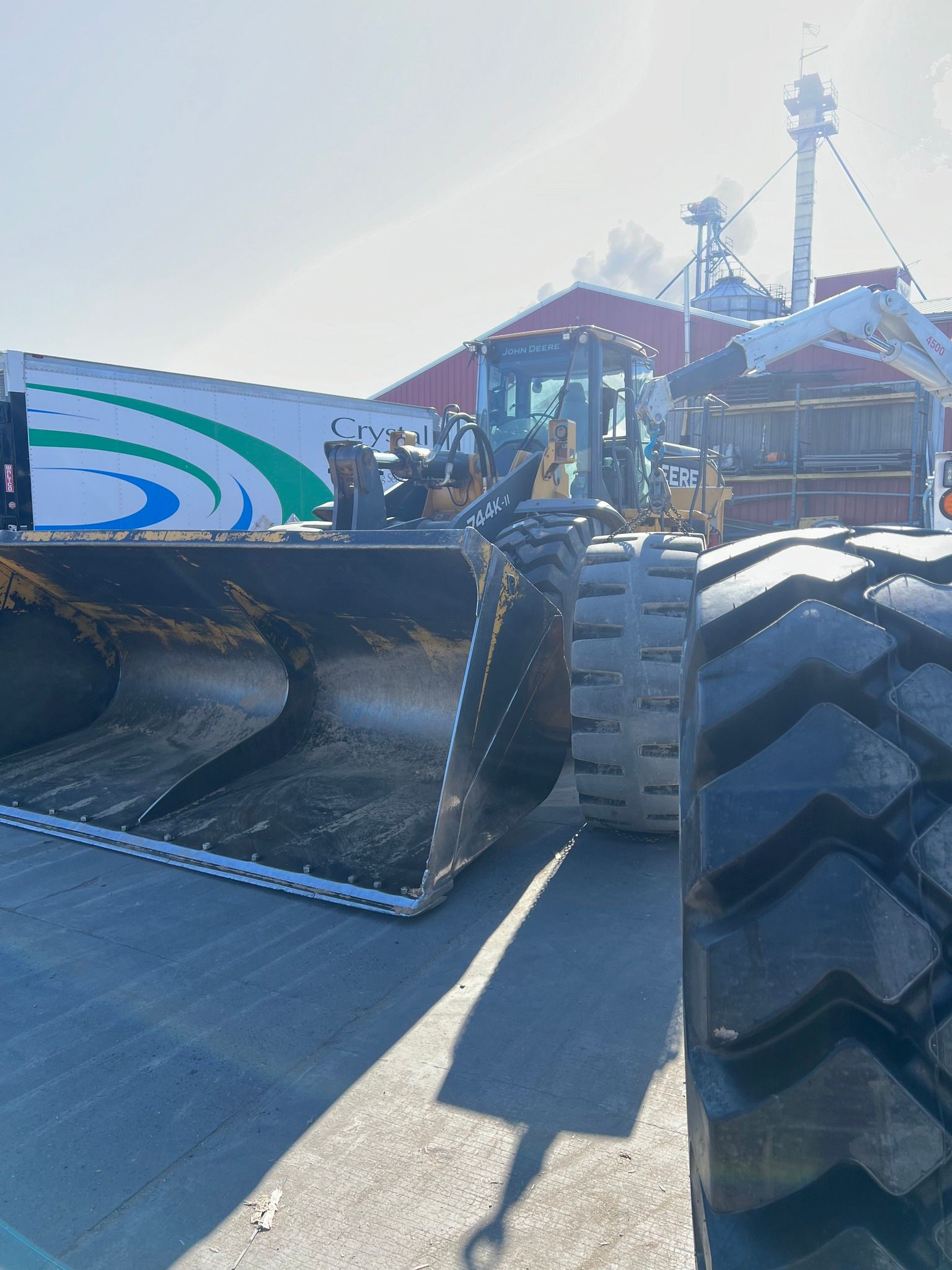 Large yellow loader, black bucket, parked near a building and truck, on a sunny day.