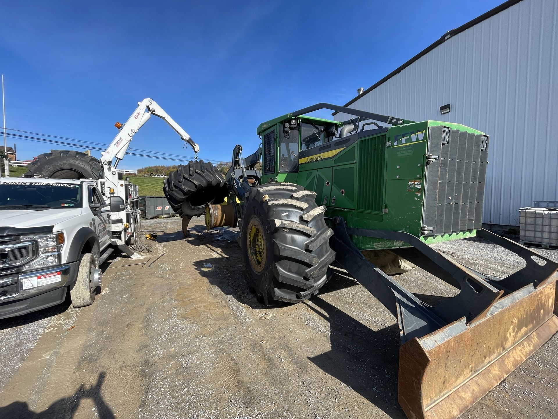Green John Deere forestry machine with large tires and a front blade, parked outside on gravel.