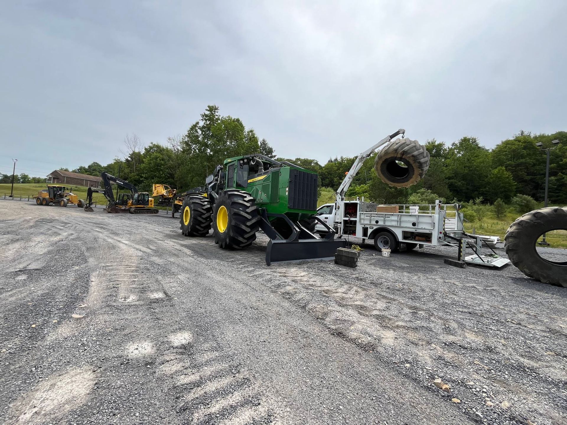 Forestry equipment parked on gravel; includes a large green John Deere tractor with tire replacement in progress.