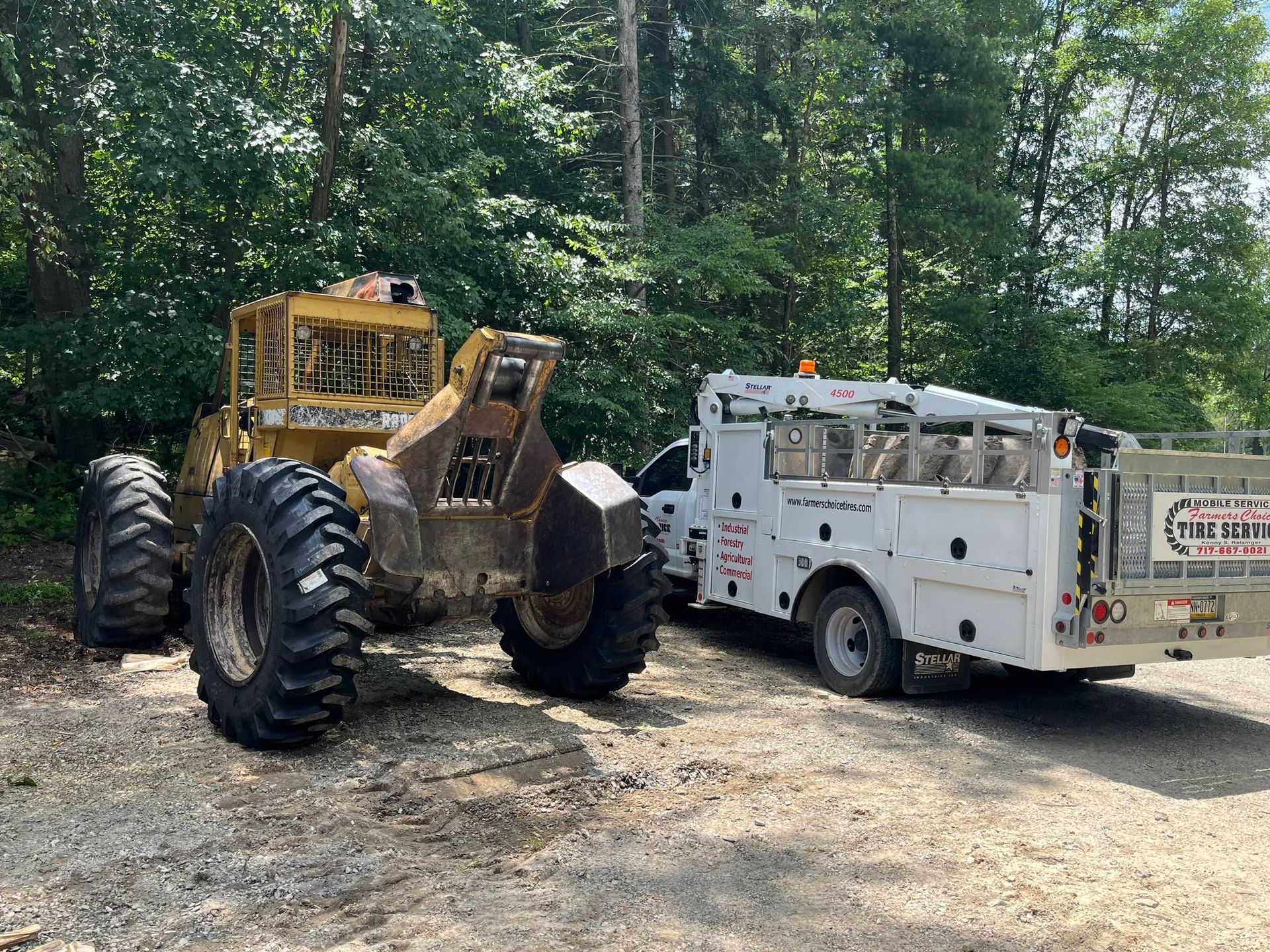 Yellow forestry machine and white service truck parked in a wooded area.