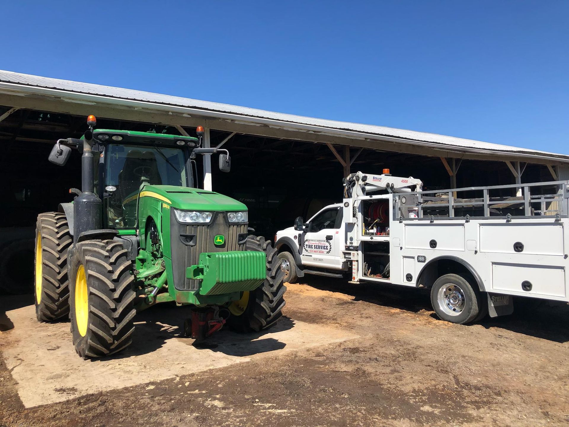 Green John Deere tractor and white service truck parked under a shed roof.