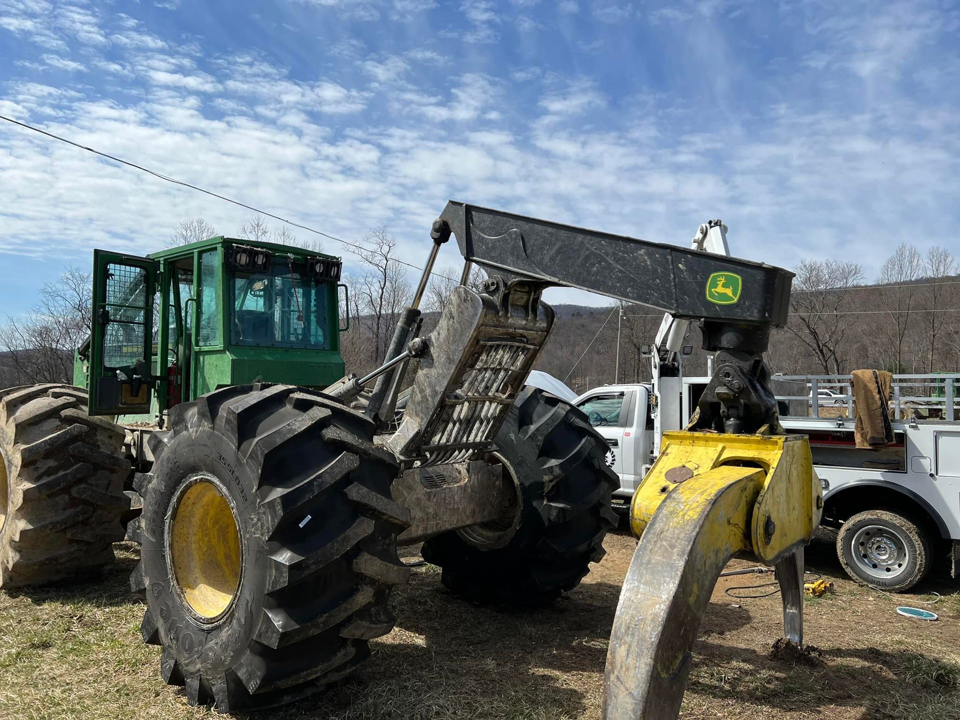 Green John Deere forestry machine with large tires and grapple arm outdoors.