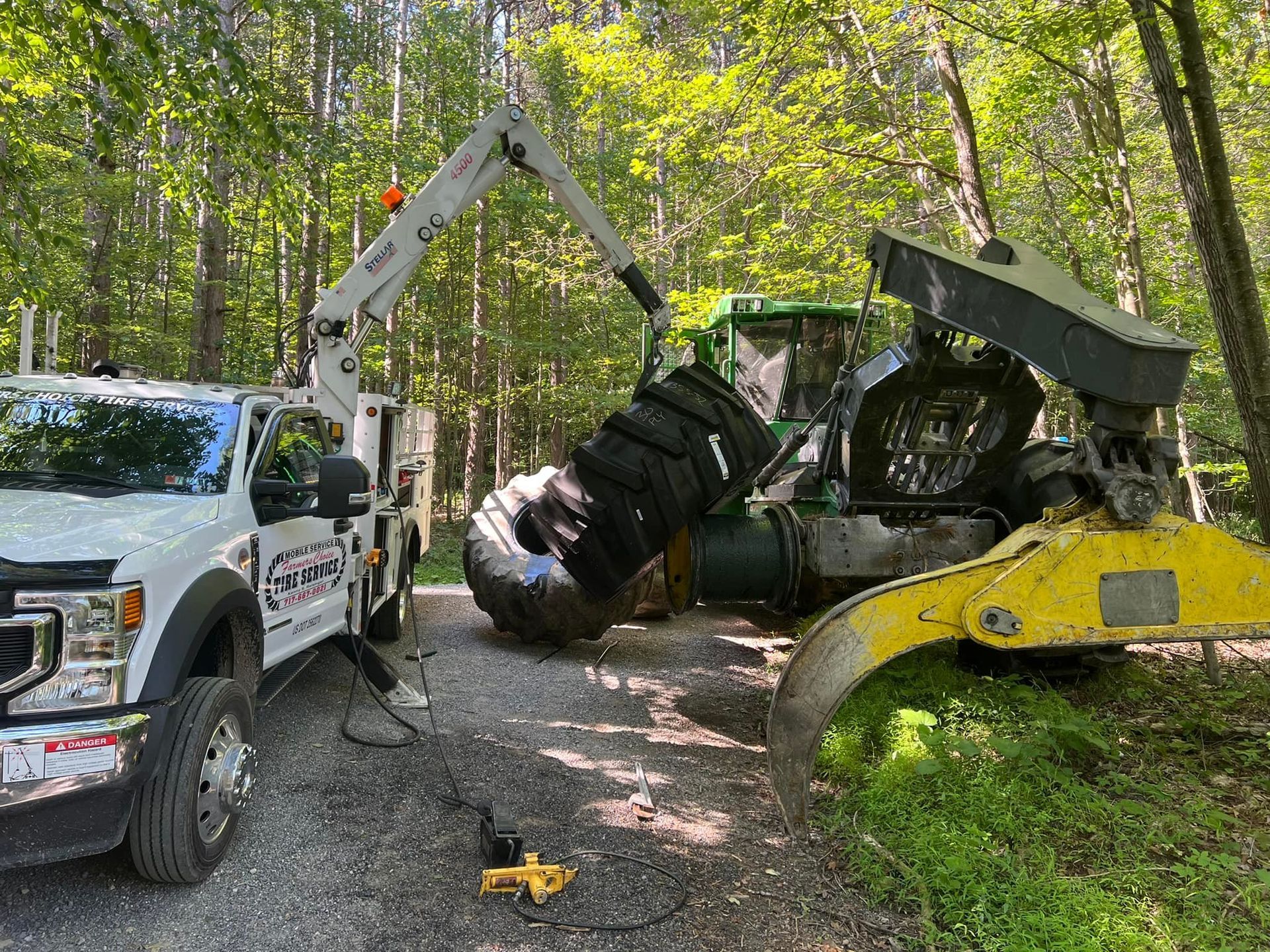White truck with crane next to large green forestry machine in a wooded area.