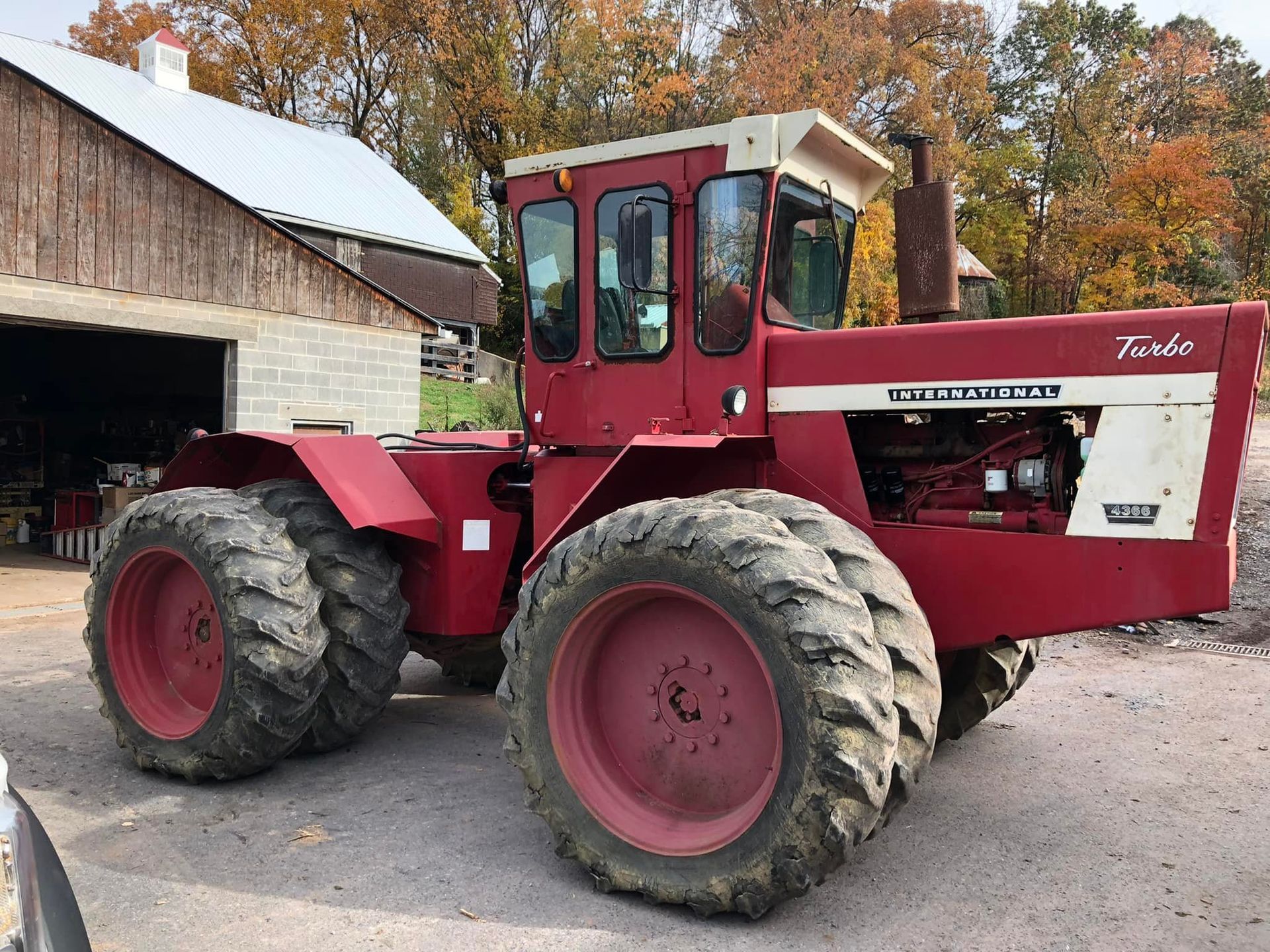 Red International Harvester tractor with white accents parked near a wooden barn, outdoors.