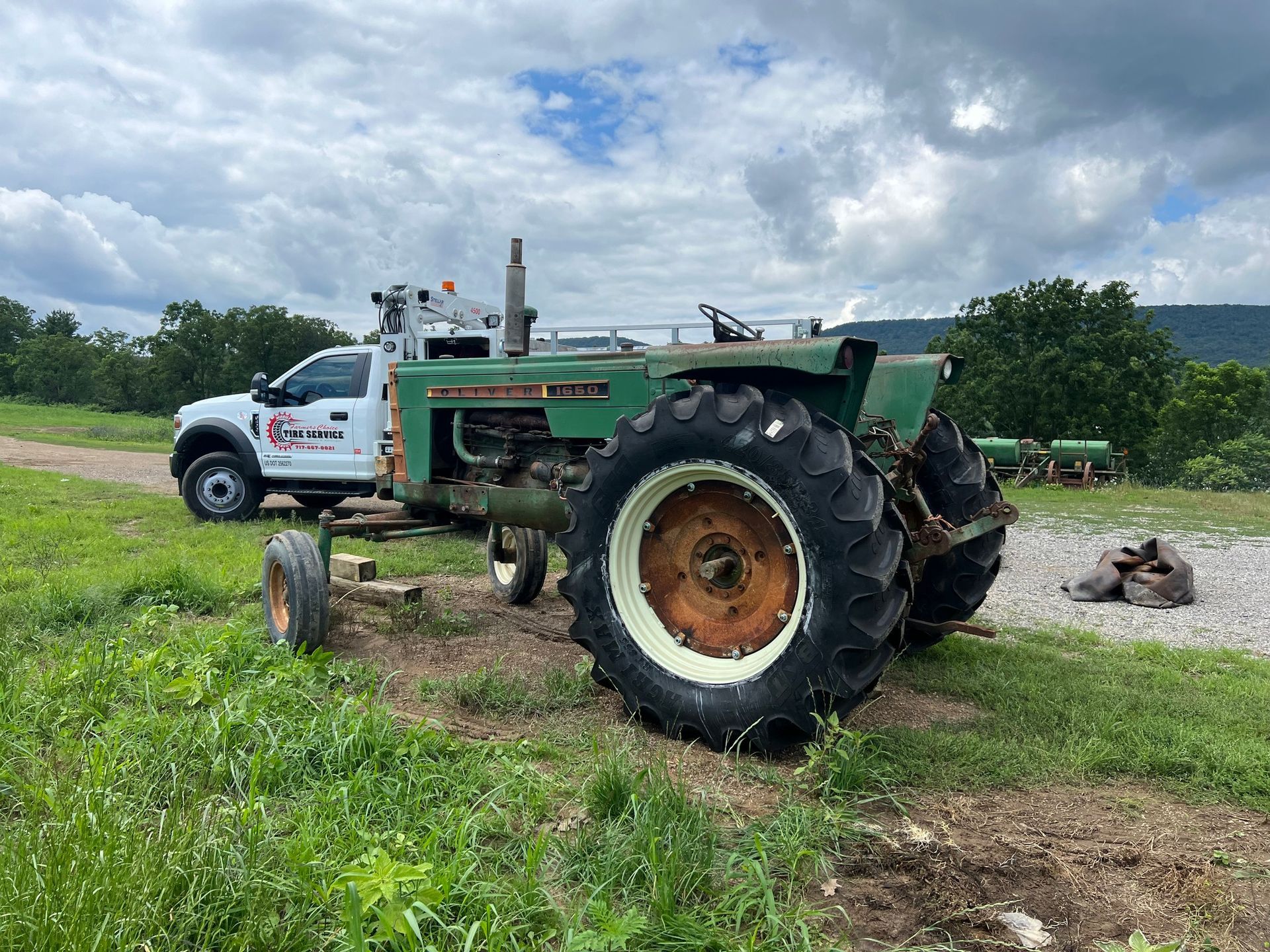 Green Oliver tractor parked next to a white service truck in a grassy field on a cloudy day.