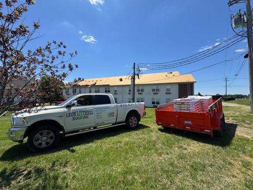 White utility truck beside a red trailer on a grassy lawn near a building under a blue sky