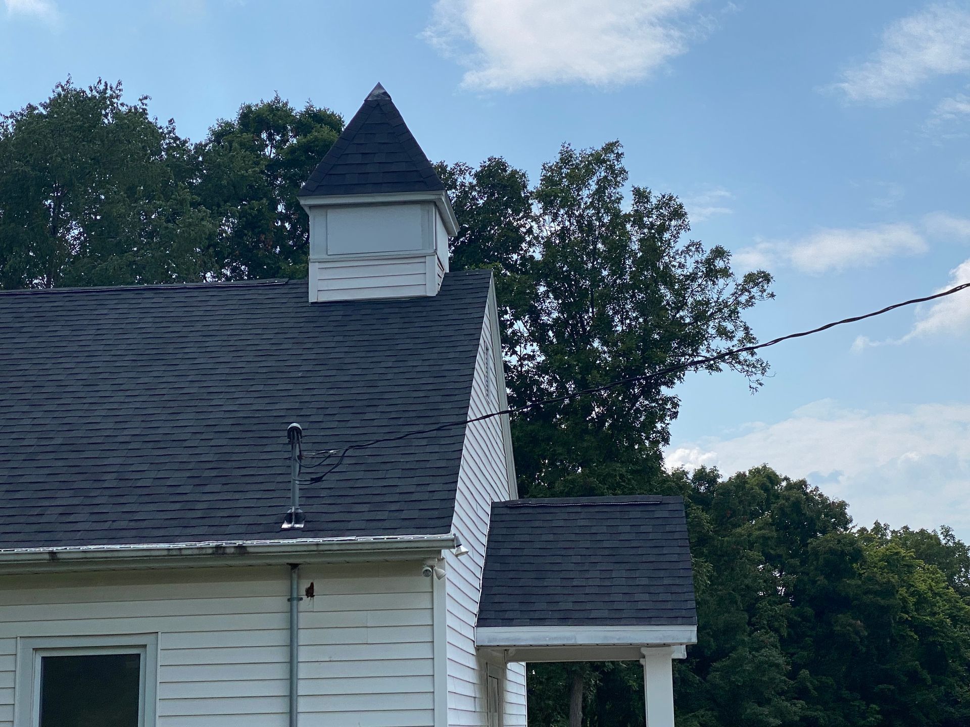 White house roof with small cupola against trees and a blue sky
