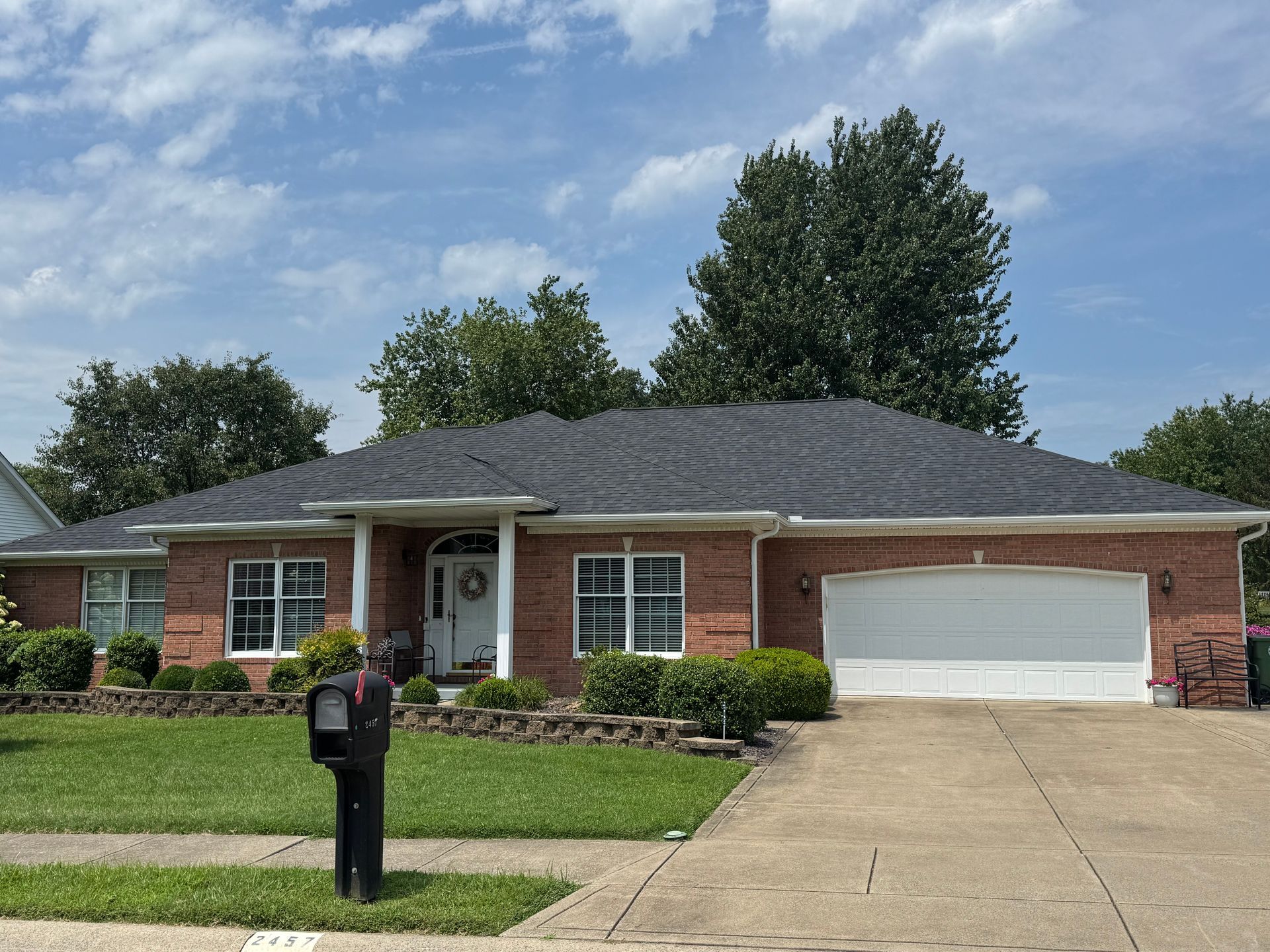 Single-story brick house with a two-car garage, driveway, and black mailbox in front.