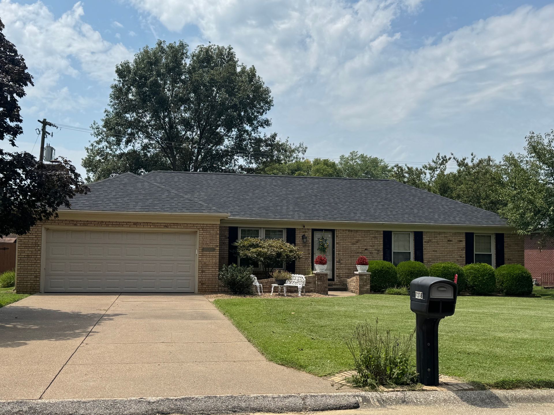 Single-story brick house with two-car garage, front lawn, and black mailbox on a sunny day