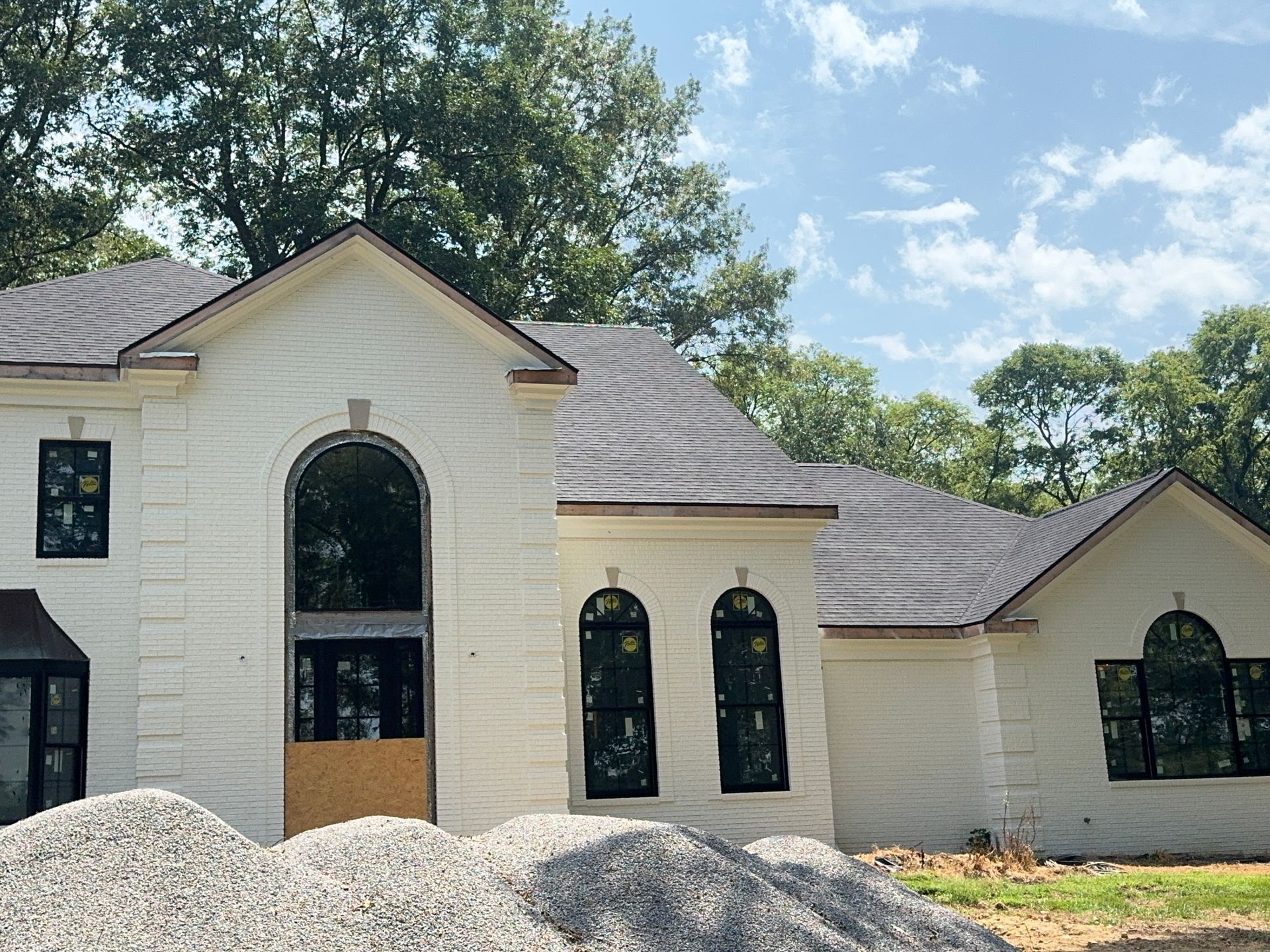 New cream-colored house with arched windows and gray roof under a blue sky