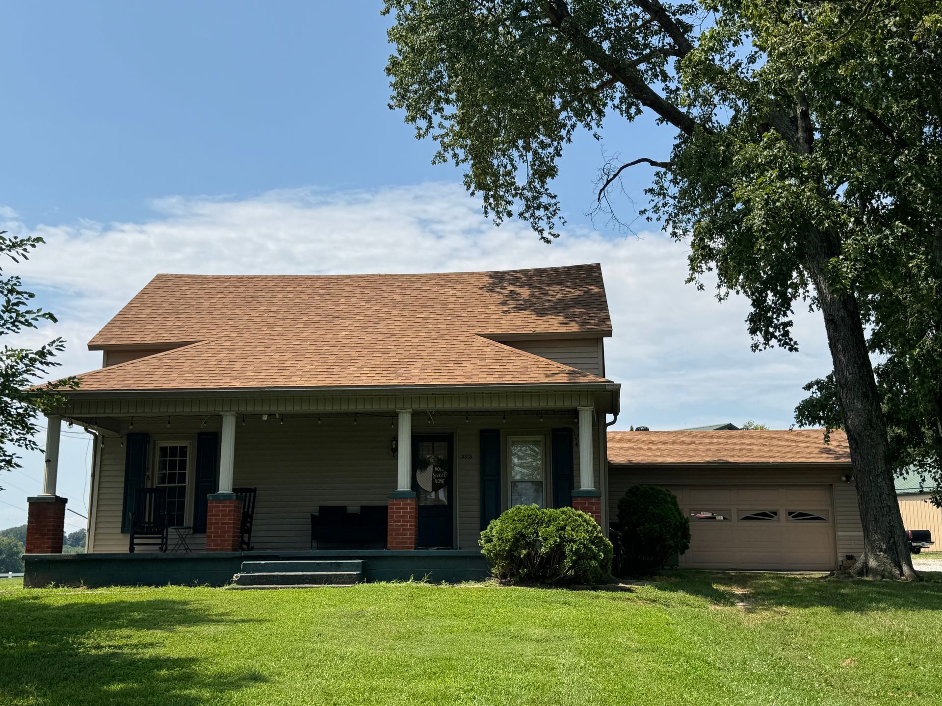 Small white house with tan roof, front porch, and attached garage on a sunny day