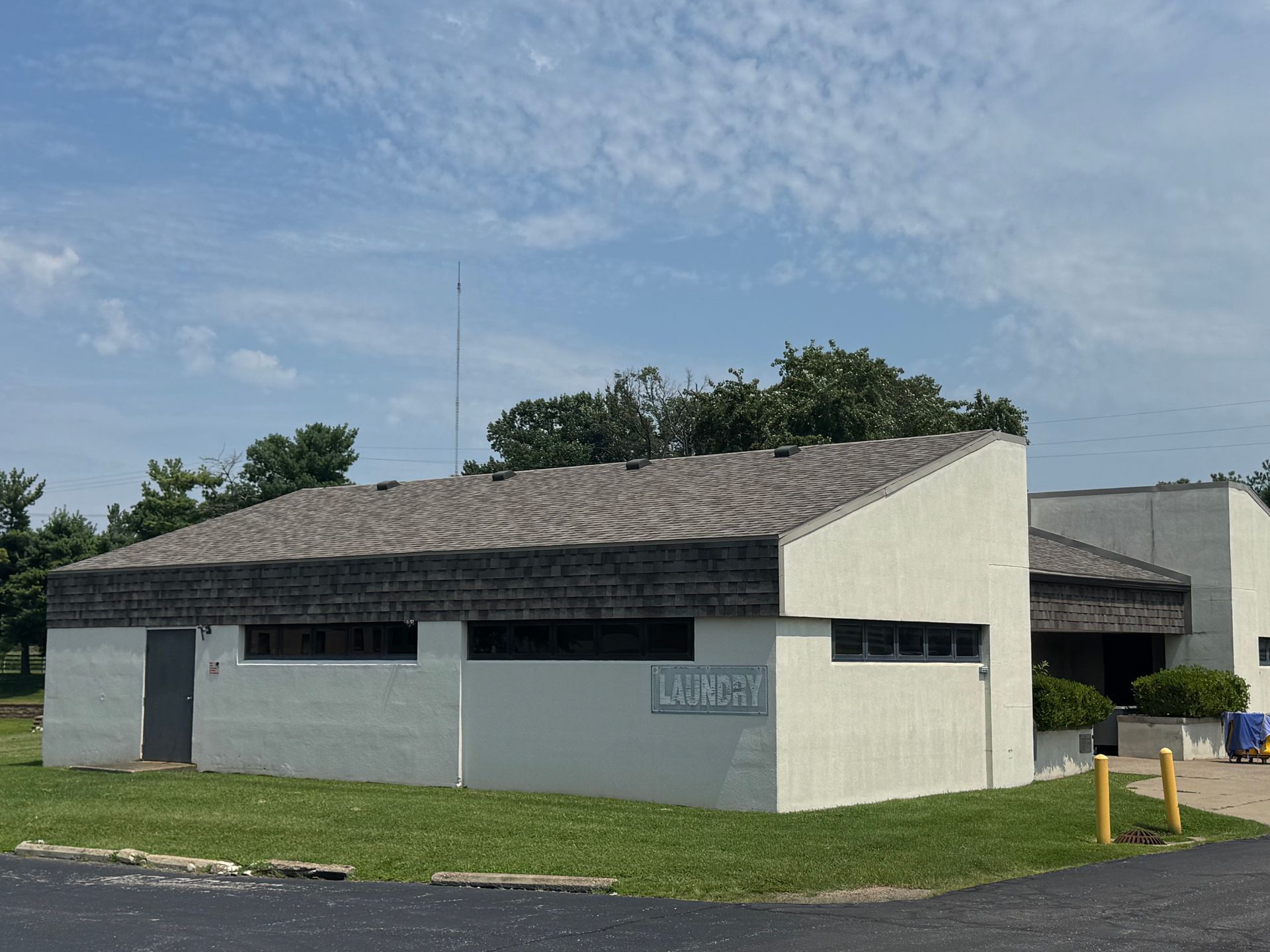 Small white building with a gray roof on a grassy corner under a cloudy sky.