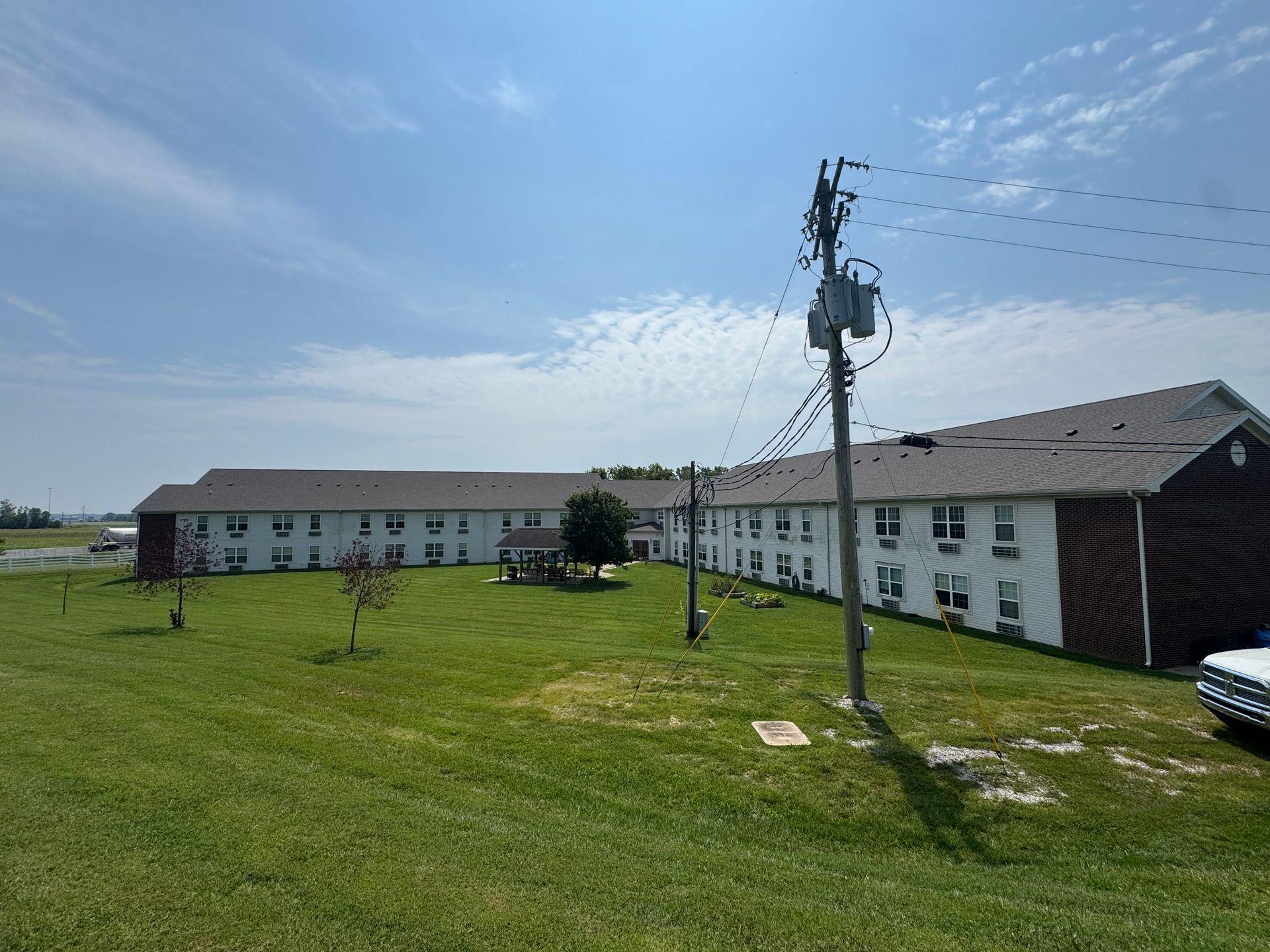 Long white apartment building beside a grassy field under a blue sky, with utility poles in front