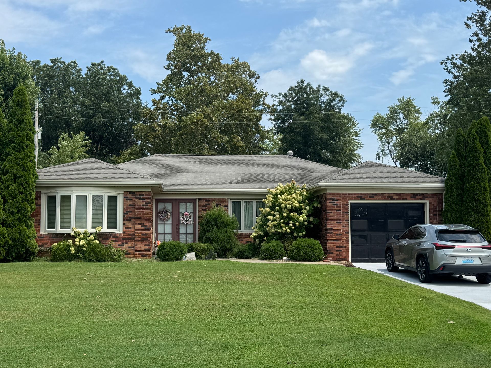 Single-story brick house with front lawn, large windows, and a car parked in the driveway