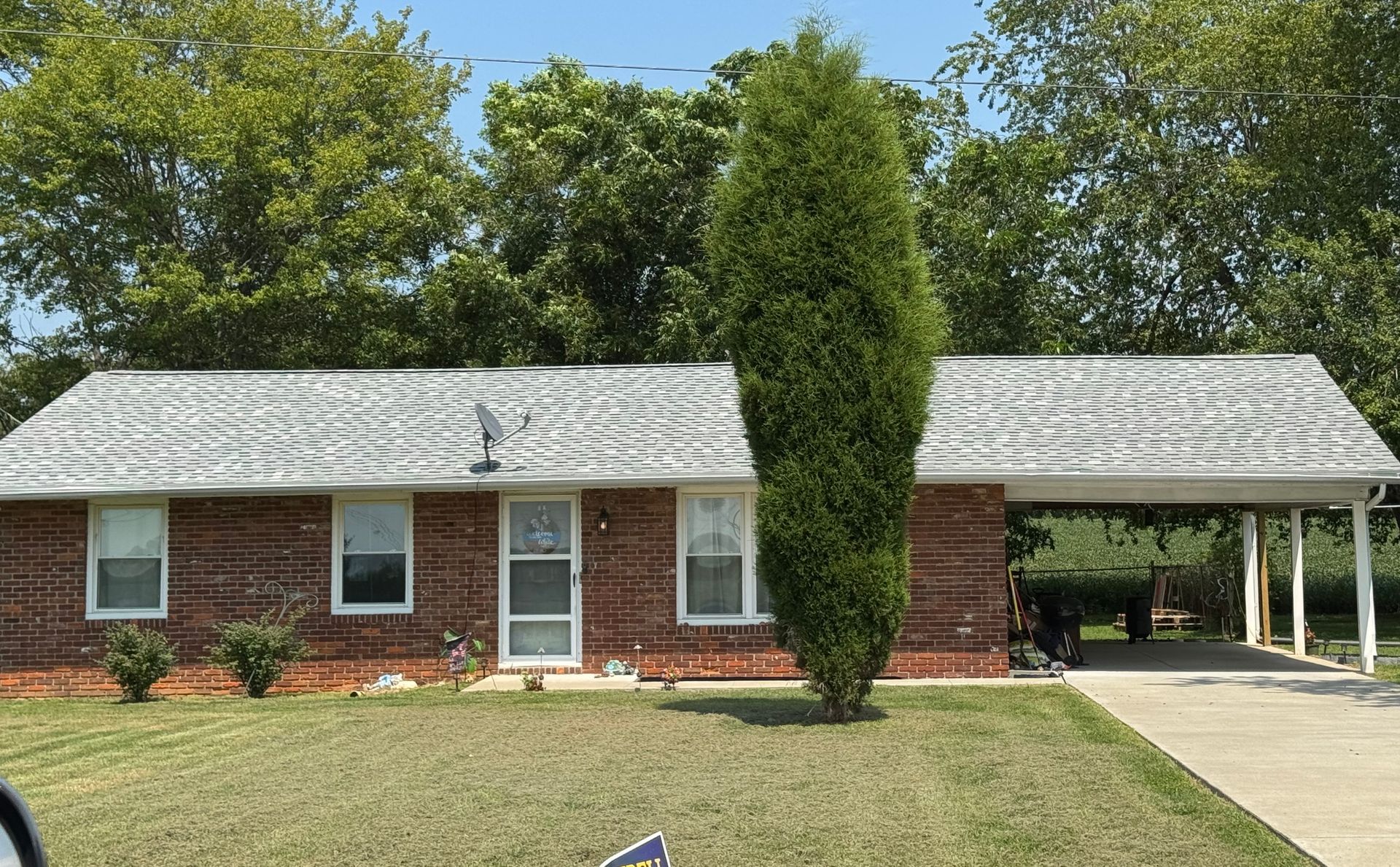 Single-story brick house with white roof, front porch, and a large tree in the front yard