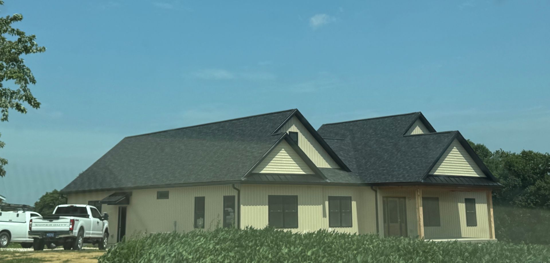 Single-story house with dark roof and light beige walls on a grassy lot under a blue sky
