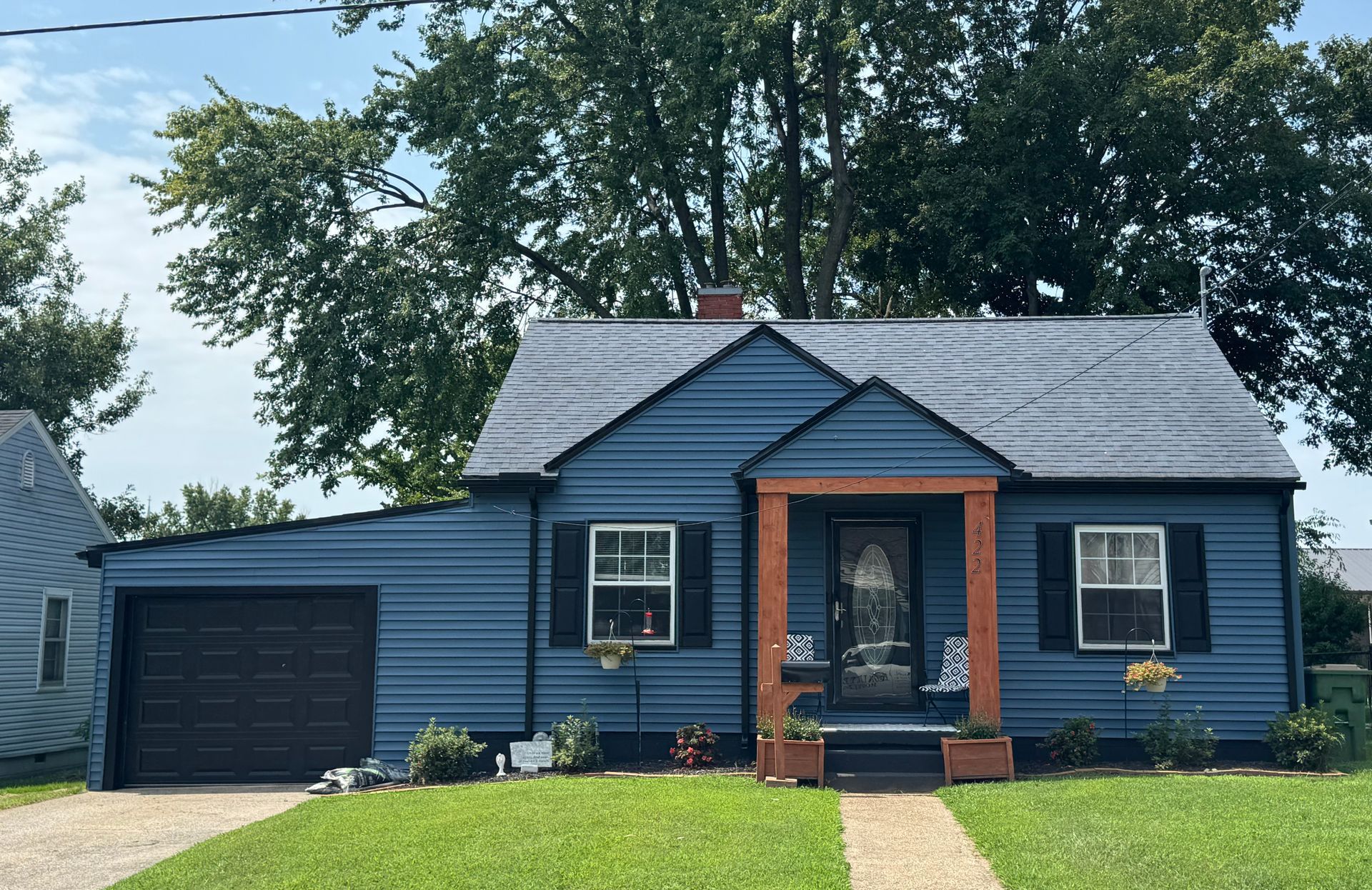 Blue house with black garage, red brick porch, and front lawn under trees