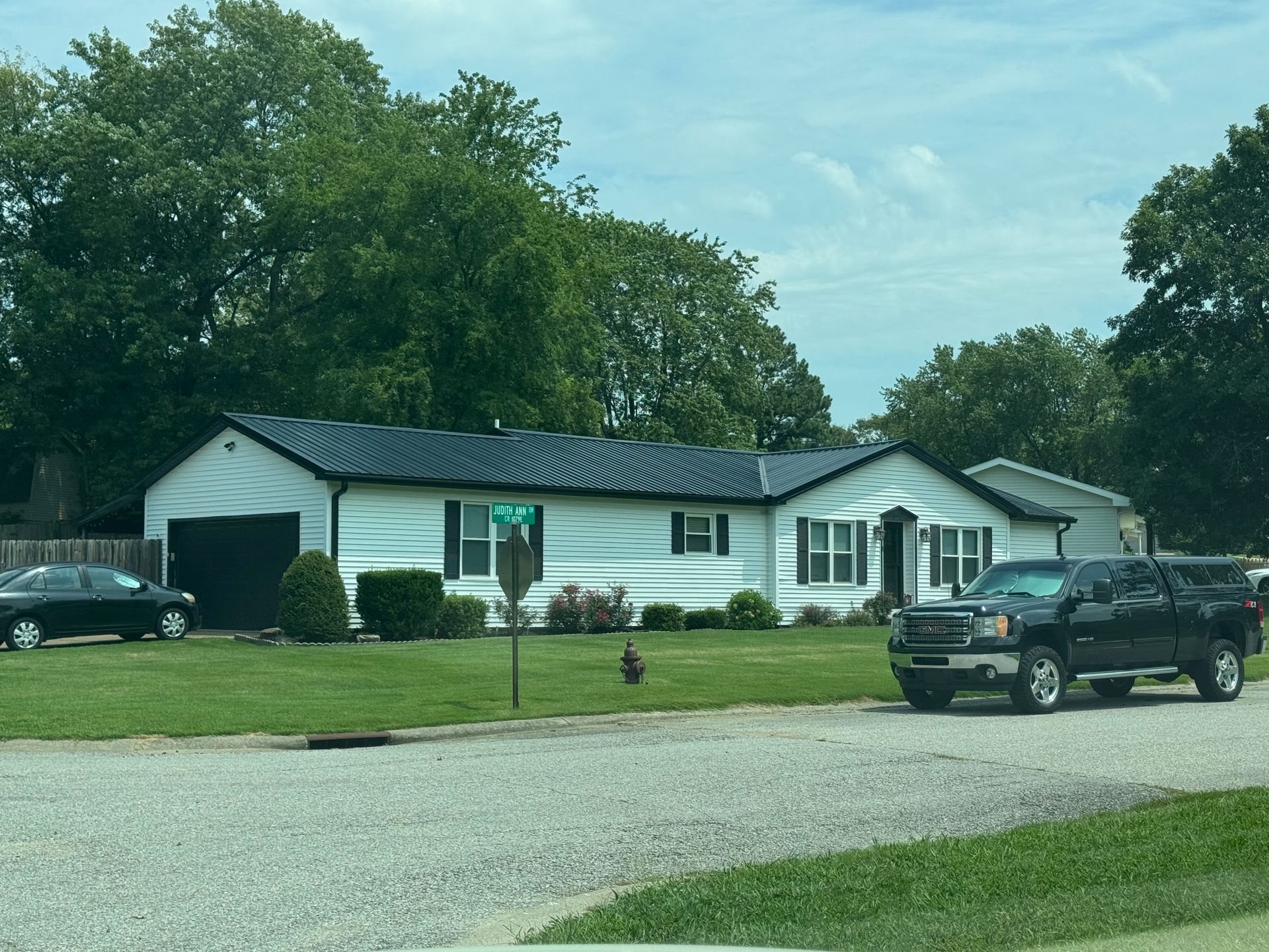 Single-story white house with black roof, parked SUV, and green lawn on a cloudy day