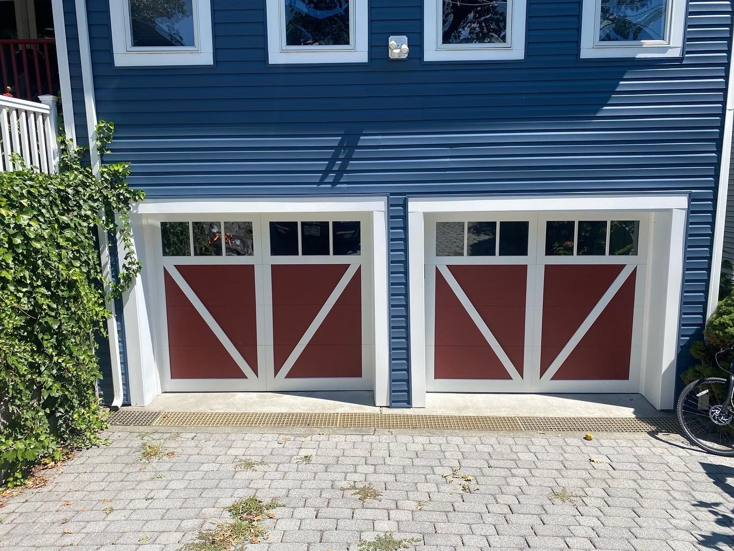 A blue house with red garage doors and a brick driveway.