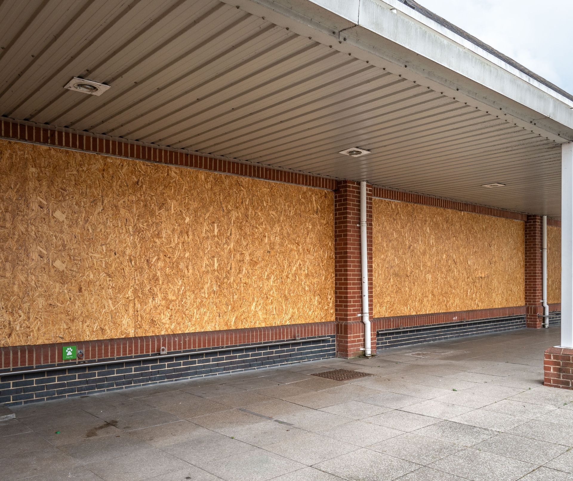 Boarded-up storefront with plywood-covered windows and brick columns under a covered walkway.