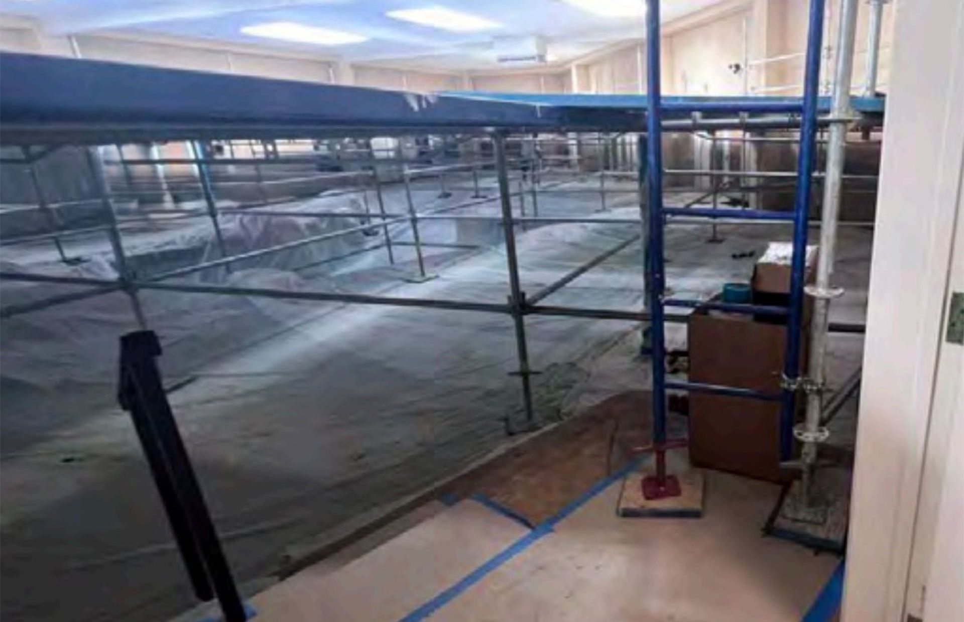 Scaffolding and tarped construction area inside a building, with blue tape marking the floor edge.
