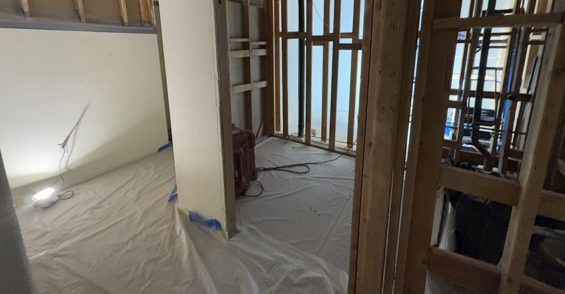 Renovation site with exposed framing, plastic-covered floors, and doorway openings in an unfinished room