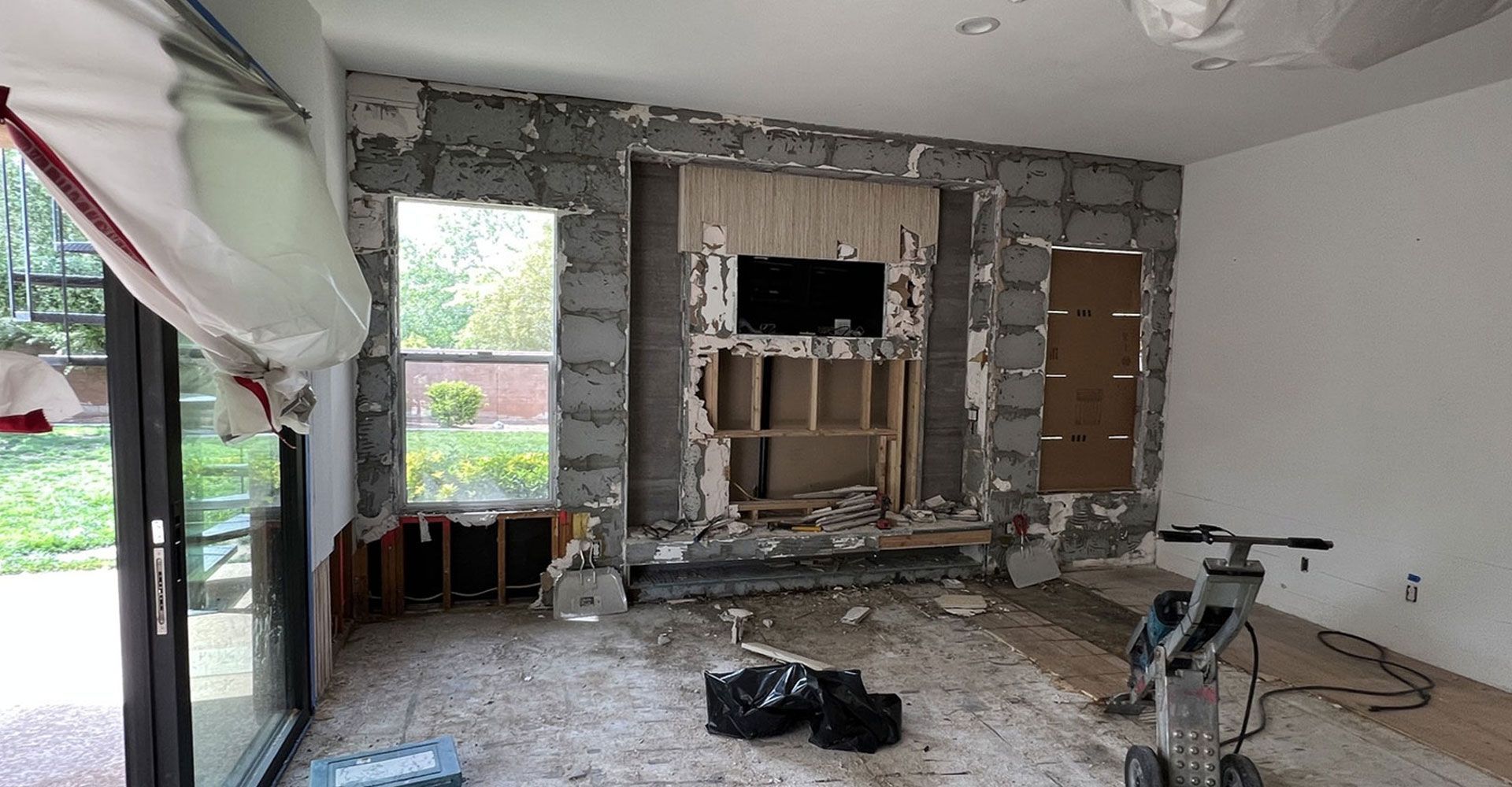 Partially renovated living room with exposed wall studs, debris on the floor, and a large window on the left