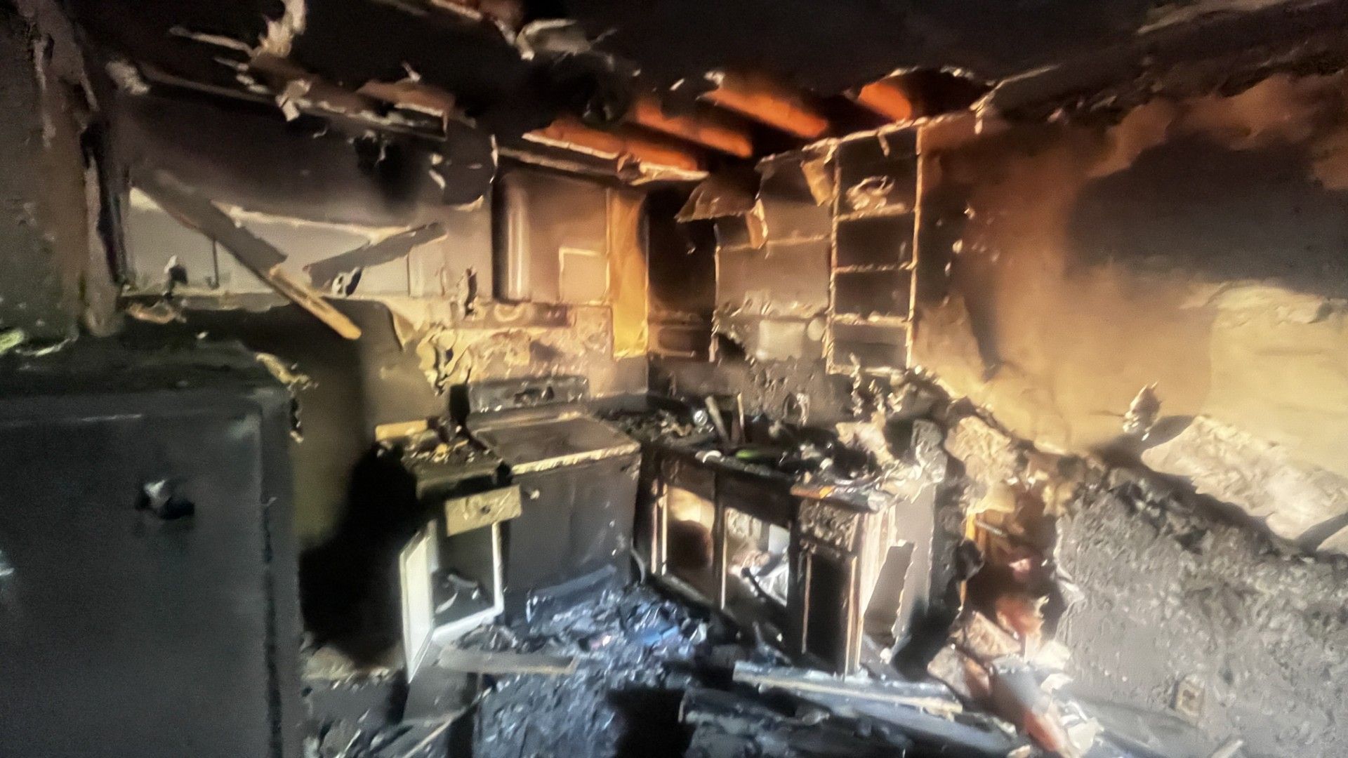 Burned kitchen with charred cabinets, collapsed ceiling, and fire damage throughout the room.
