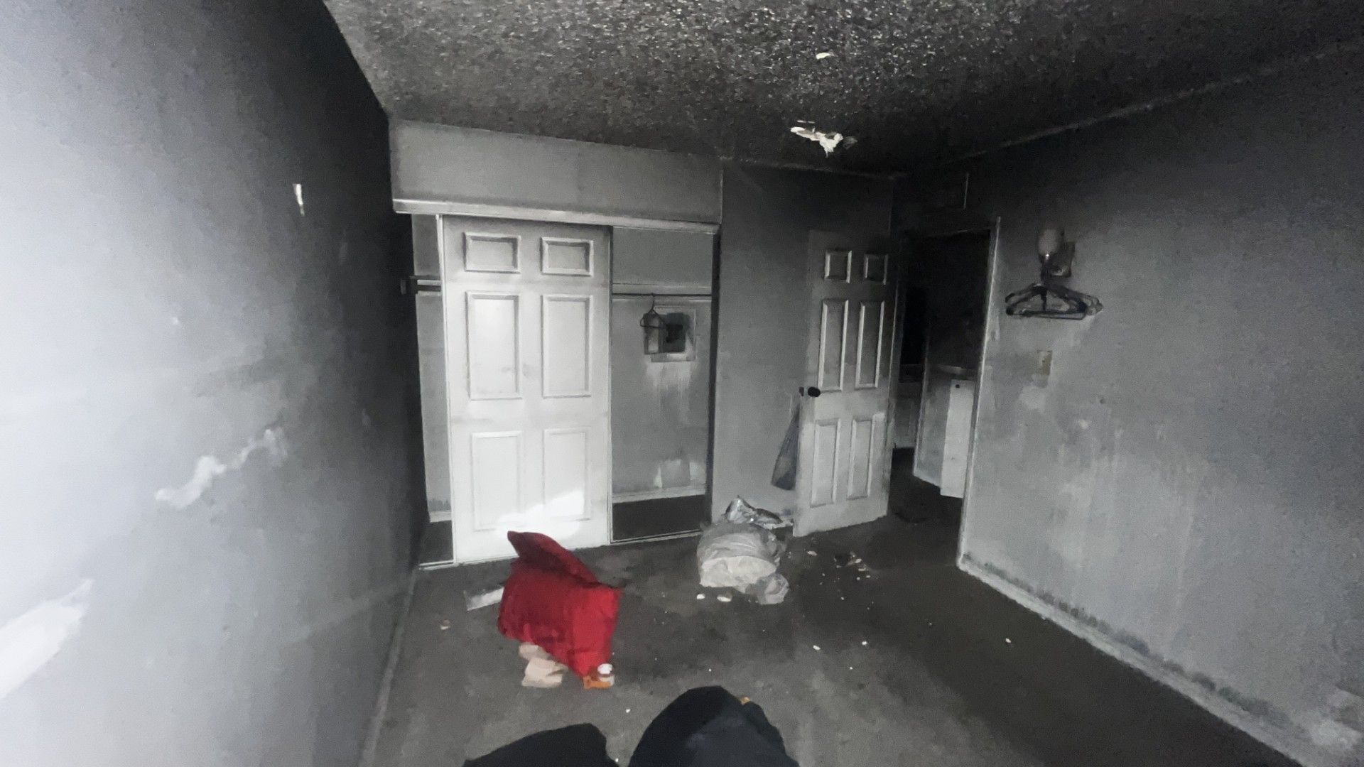 Dim, damaged room with a white door, scattered debris, and a red chair in the foreground.