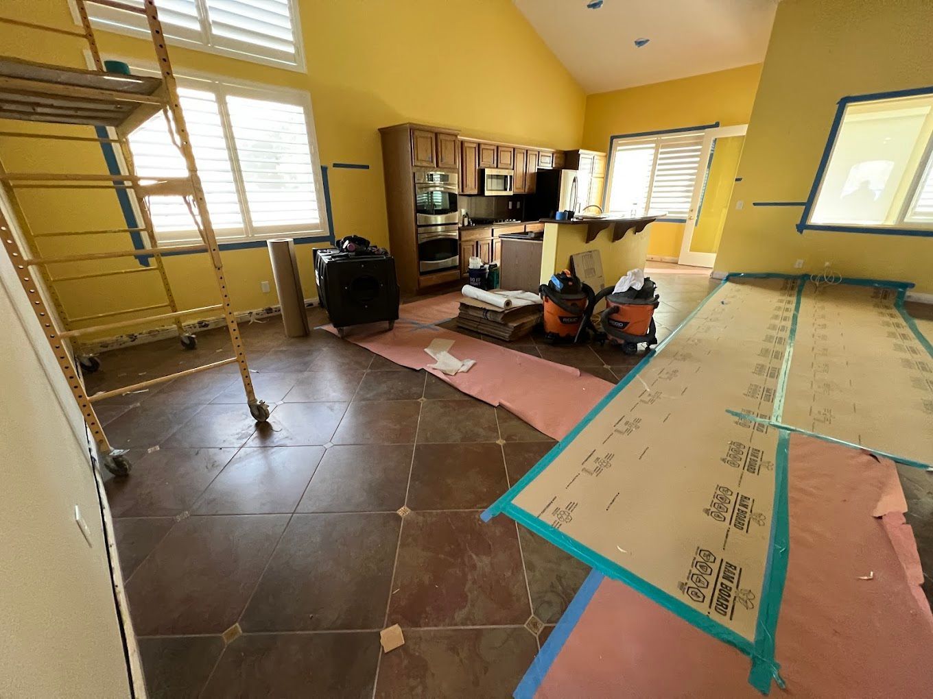 Yellow room under renovation with floor coverings, scaffolding, tools, and built-in shelves.