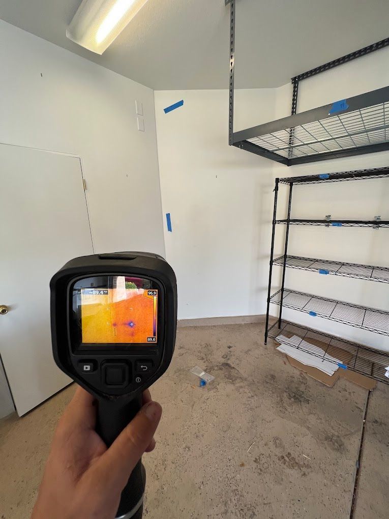 Handheld thermal camera aimed at a white room with metal shelving and an open door.