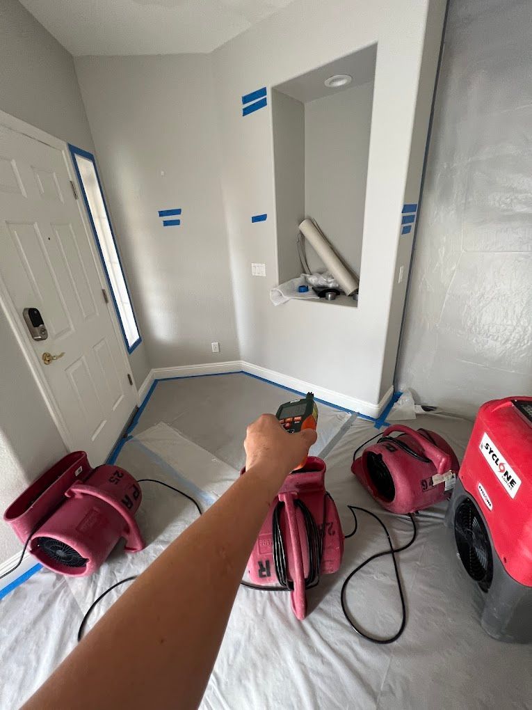 Painted room with wall cutouts, tool bags, and a person’s arm holding a power tool near the floor