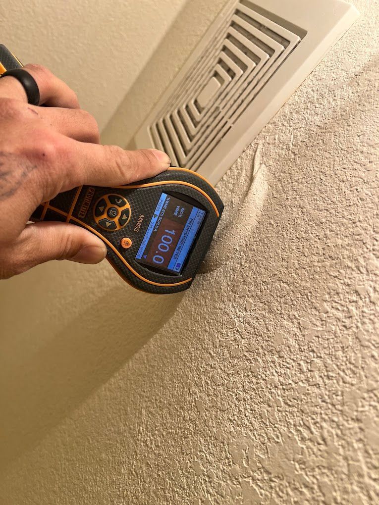 Handheld air-quality meter checking a ceiling vent in a beige room